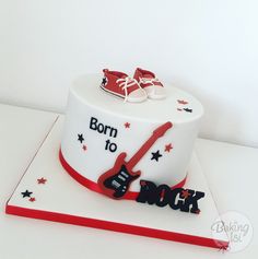 a white cake with red and black decorations on it's side, topped with a guitar