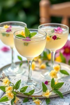 two glasses filled with drinks sitting on top of a table next to flowers and greenery