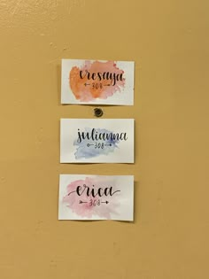 three watercolor paper tags hanging on a wall with the names of two different countries