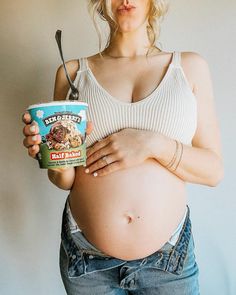 a pregnant woman holding a cup of yogurt with a spoon in her hand