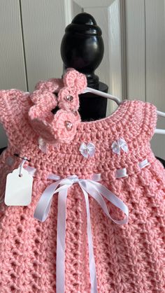 a pink crocheted baby dress with white bows and tags on the collarline