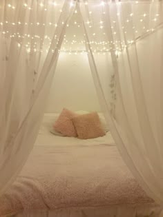 there is a bed with white curtains and lights on the headboard in this bedroom