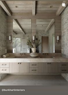 a large bathroom with stone walls and wooden ceilinging is pictured in this image, there are two sinks on either side of the mirror