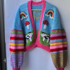 a colorful knitted sweater hanging up on a white wall with a rainbow and mushroom design