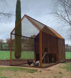 a chicken coop in the middle of a field with two chickens inside and one on the ground