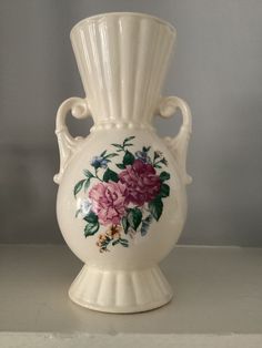 a white vase with pink flowers painted on the side and green leaves in the middle