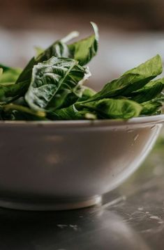 a white bowl filled with green leaves on top of a table