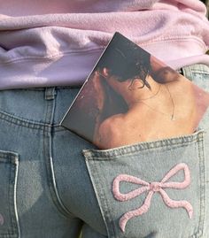 a woman's jeans with a pink bow on the back pocket and an album in her pocket