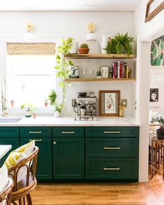 a kitchen with green cabinets and white counter tops, plants on the shelf above the sink