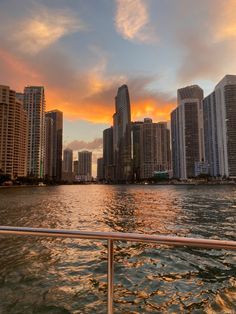 the sun is setting in front of some tall buildings on the water with boats passing by