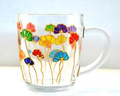 a glass coffee cup with colorful flowers painted on the outside and inside, sitting on a white surface