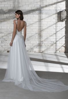 a woman in a white wedding dress standing against a brick wall with her back to the camera