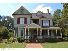 a large gray house with red shutters on the front and second story, surrounded by lush green trees