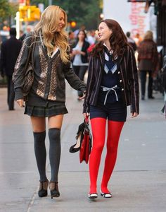 two young women walking down the street holding hands and talking to each other while wearing red tights