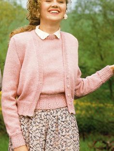 a woman wearing a pink sweater and flowered skirt holding an umbrella in her hand