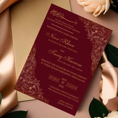 a red and gold wedding card on top of a table next to some white flowers