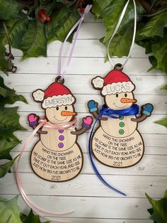 two wooden snowmen with christmas hats on their heads and name tags attached to them