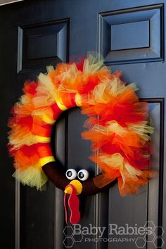 an orange and yellow wreath with a turkey face on it's head hanging from the front door