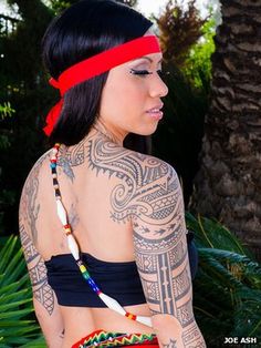 a woman with tattoos on her chest and arm holding a pencil in her hand while standing next to a palm tree