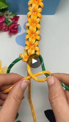 someone is working on some yellow and green string art work with flowers in the background