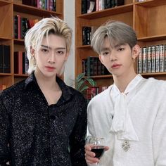 two young men standing next to each other in front of bookshelves holding wine glasses