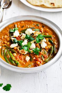 a bowl filled with green beans and cheese next to some pita bread on a white table