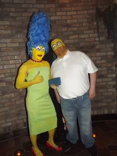 a man and woman dressed up as simpsons and the simpsons costumed characters pose for a photo in front of a brick wall