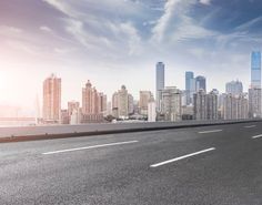 an empty highway in front of a large city with tall buildings on both sides and blue sky