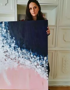 a woman holding up a large painting with white and blue paint on it's sides