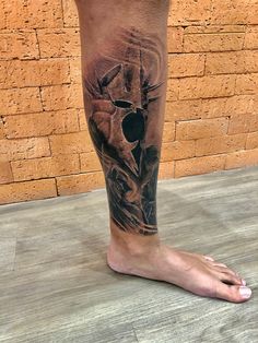 a man's leg with a skull and cross tattoo on his left calf, next to a brick wall