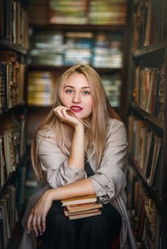 a woman is sitting in a library with books on the shelves and looking at the camera