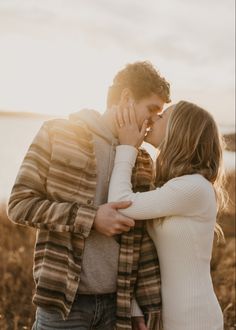 a man and woman kissing each other while standing in front of a body of water