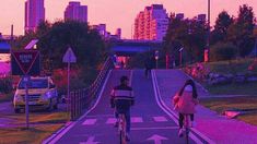 two people riding bicycles down the street in front of a city skyline at sunset with pink hues