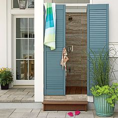 blue shutters open on the front door of a white house with potted plants