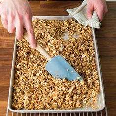 a person scooping granola into a pan with a blue spatula on top