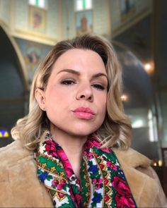 a woman with blonde hair wearing a fur coat and colorful scarf in a large building