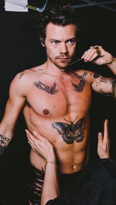 a shirtless man with tattoos on his chest is holding something in his hand and looking at the camera