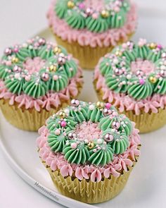 four cupcakes decorated with green and pink icing on a white platter