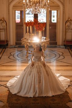 a woman in a wedding dress standing on the floor with a chandelier above her head