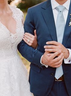 the bride and groom are standing close together in their wedding attire, holding each other's hands