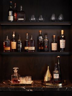 several bottles and glasses on shelves in a room with marble counter tops, black walls