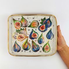 a hand holding a decorative plate with fruit on it