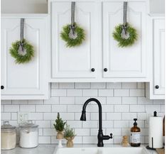 two wreaths hanging from the kitchen cabinets above a sink with greenery on it