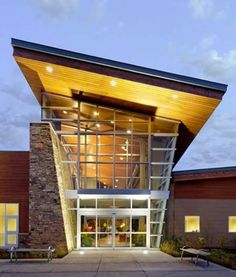 the front entrance to a building with lights on and benches in front of it at night