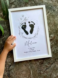 a child's hand is holding up a framed photo with the baby's footprints on it