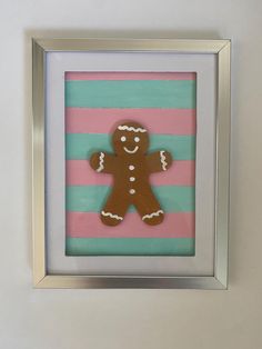 a gingerbread cutout in a silver frame on a pink and blue striped wall