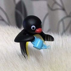 a toy penguin with a blue cup in it's mouth sitting on some white fur