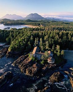 an aerial view of a house surrounded by trees and water with mountains in the background