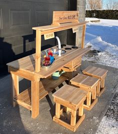 a wooden picnic table with benches in front of a garage door and snow on the ground