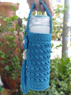 a hand holding a blue crocheted cup holder with a straw in the bottom